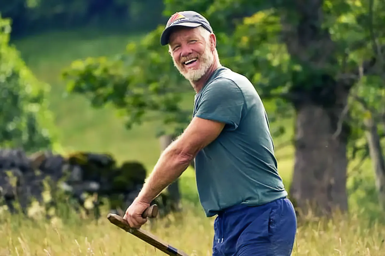 Kevin wearing blue clothes and cap, scything, smiling at camera
